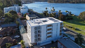 A multi-story hotel with a flat roof, located near a body of water with boats. - Coastal 3-Bed Retreat Near Batemans Bay (Batemans Bay)