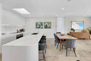 A modern kitchen with a central island, dining table with chairs, and artwork on the walls. - Coastal 3-Bed Retreat Near Batemans Bay (Batemans Bay)