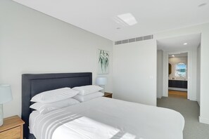 Ein modernes Schlafzimmer mit einem großen Bett, einem Nachttisch mit Lampe, einem Wandbild und Blick ins Badezimmer.