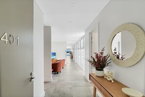A hallway with a number sign, a round mirror, a console table with a plant, and a view to a room with a sofa and a TV. - Coastal 3-Bed Retreat Near Batemans Bay (Batemans Bay)