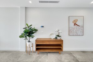 A minimalist room with a wooden console table, a potted plant, a wall-mounted thermostat, and a framed artwork. - Coastal 3-Bed Retreat Near Batemans Bay (Batemans Bay)