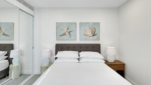 A bedroom with a bed, two bedside tables with lamps, a nightstand, a mirror, and two wall-mounted paintings of a starfish and a shell. - Coastal 3-Bed Retreat Near Batemans Bay (Batemans Bay)