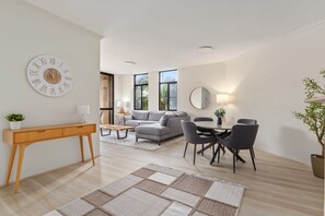 Ein modernes Wohnzimmer mit einer Couch, einem Esstisch, Stühlen, einem Konsolentisch, einer Uhr und einem großen Fenster.