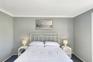 Une chambre à coucher avec un lit, des tables de chevet blanches, un tableau accroché au mur et un plafond blanc.
