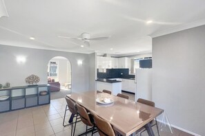 A modern dining area with a large table, chairs, and a ceiling fan. - Family 3-Bed Retreat Near Batehaven Beach (Batehaven)