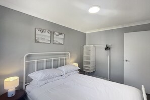 A bedroom with a bed, bedside lamp, wall art, and a wardrobe. - Family 3-Bed Retreat Near Batehaven Beach (Batehaven)