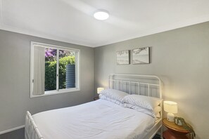 A bedroom with a bed, a nightstand, a lamp, a window with curtains, and two wall-mounted pictures. - Family 3-Bed Retreat Near Batehaven Beach (Batehaven)