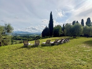 A grassy outdoor area with lounge chairs and a table, overlooking a scenic landscape with trees and distant hills. - Luxury Villa with Panoramic Terrace - 5 rooms (Toscana)