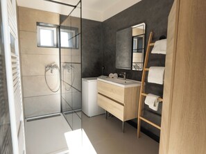 Een moderne badkamer met een glazen douchecabine, een houten wastafelmeubel en een spiegel.