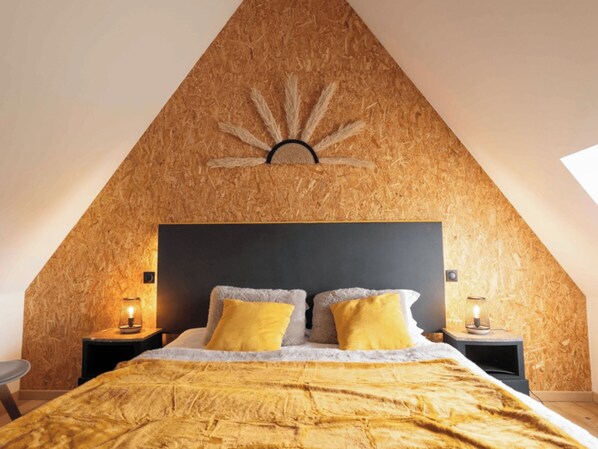 A bedroom with a sloped ceiling, a bed with a textured blanket, two bedside lamps, and a wall-mounted sun decoration.