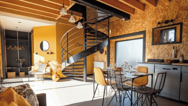 A modern kitchen with a built-in stove, a dining area with a round table and chairs, and a spiral staircase leading to an upper level. - L'Atelier Vacation Rental (Wierre-Effroy)