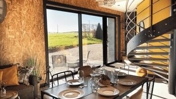 Een eetgedeelte met een tafel voor vier personen, een spiraaltrap en een groot raam met uitzicht op een grasveld.