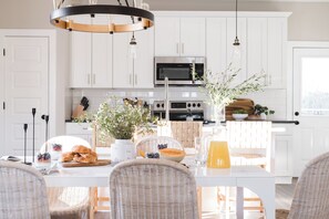 Une cuisine moderne avec des meubles blancs, des appareils en acier inoxydable, des chaises en osier et une table à manger préparée pour le petit-déjeuner.
