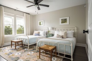 Ein Schlafzimmer mit zwei Betten, einem Deckenventilator, einem kleinen Holzschemel und einem floralen Teppich.