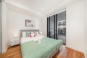 A modern bedroom with a large bed, a nightstand, a wall-mounted artwork, and a sliding glass door leading to a balcony. - Cozy 2B2B Apartment In Burwood (Burwood)