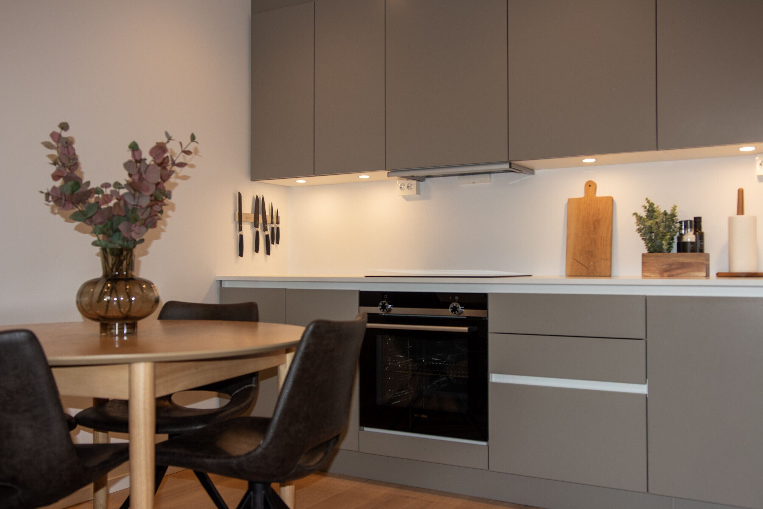 A modern kitchen with a dining table, chairs, an oven, and a wooden cutting board on the counter.