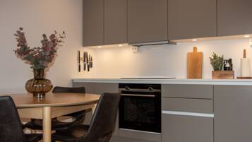 A modern kitchen with a dining table, chairs, an oven, and a wooden cutting board on the counter.