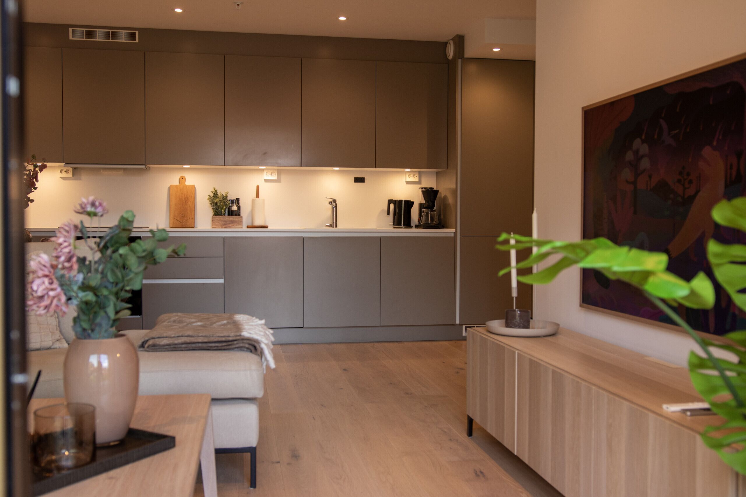 A modern kitchen with a central island, a dining area with a bench, and a painting on the wall.