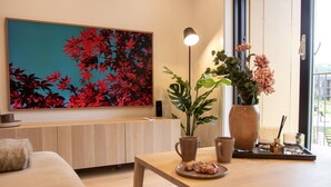 Un salon moderne avec un canapé en bois, une table basse sur laquelle sont disposées des pâtisseries, un grand tableau représentant des fleurs, une plante en pot et un vase rempli de fleurs.