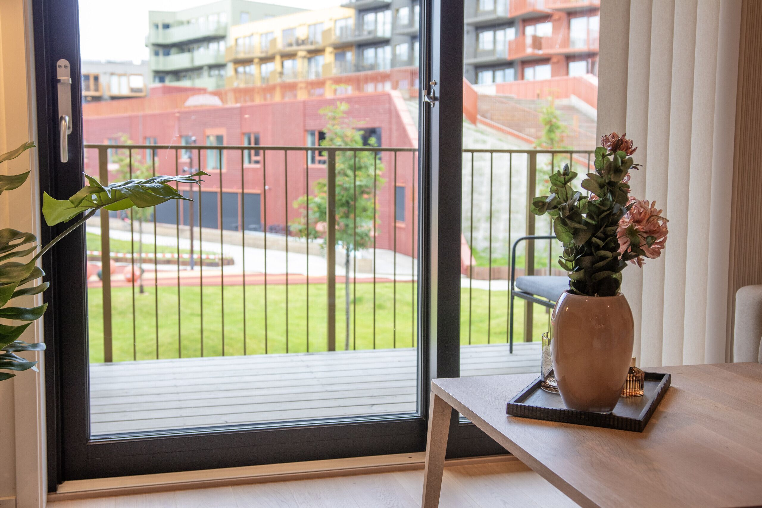 A room with a sliding glass door to an outdoor area, a potted plant, and a vase with flowers on a tray.