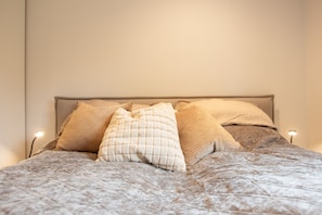 Cama com cobertura acolchoada, duas luminárias de cabeceira e vários travesseiros.