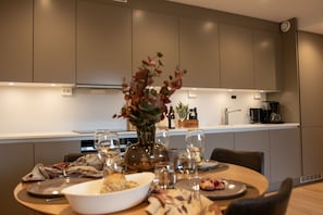 Una cucina moderna con un tavolo da pranzo per due persone, dotata di macchina da caffè, bicchieri da vino e un vaso con fiori.