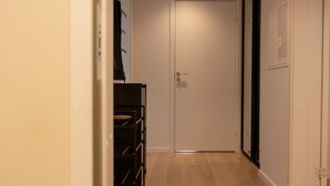 Un couloir étroit avec un plancher en bois, une porte blanche au fond et un présentoir noir avec des étagères sur le côté gauche.