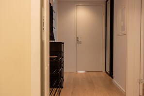 A narrow hallway with a wooden floor, a white door at the end, and a black rack with shelves on the left. - Aurora Arctic Apartment (Tromsø)