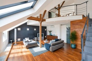 Ein geräumiges Loft mit hohen Decken, einer Holztreppe und einer modernen Wohnbereich mit Sofas und einem Couchtisch.