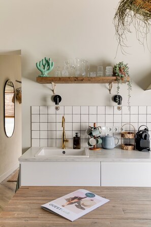 A kitchen with white tiles, a sink, a wooden countertop, and a magazine on a table.