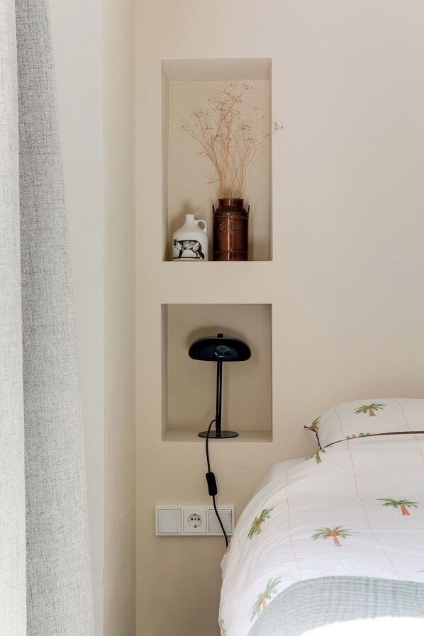 A bedroom with a bed, a wall-mounted shelf with a vase and a teapot, and a floor lamp.