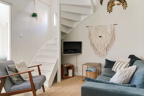 A modern living room with a staircase, a flat-screen TV, and a macrame wall hanging.