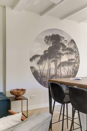 A dining area with a round wall mural, a wooden table, black chairs, a small side table with a basket, and a blue sofa.