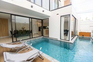 Ein moderner, überdachter Pool mit Glaswänden, Liegestühlen und einem sichtbaren Küchenbereich.