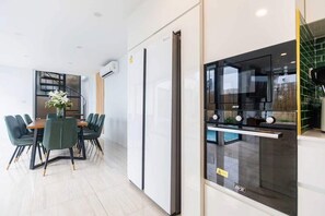 Eine moderne Küche mit einem schwarzen Kühlschrank, einem Backofen mit Glastür sowie einem Essbereich mit einem Holztisch und grünen Stühlen.