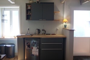 Eine kompakte Küche mit Kühlschrank, einer kleinen Ablage und einem Fenster mit Tageslicht.