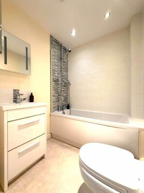 A modern bathroom with a white vanity, a bathtub, and a toilet. - Cheltenham Town Centre 2-Bed 2-Bath Flat + Parking (Cheltenham)