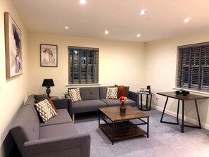 A living room with a sofa, coffee table, and a small table with a lamp. - Cheltenham Town Centre 2-Bed 2-Bath Flat + Parking (Cheltenham)