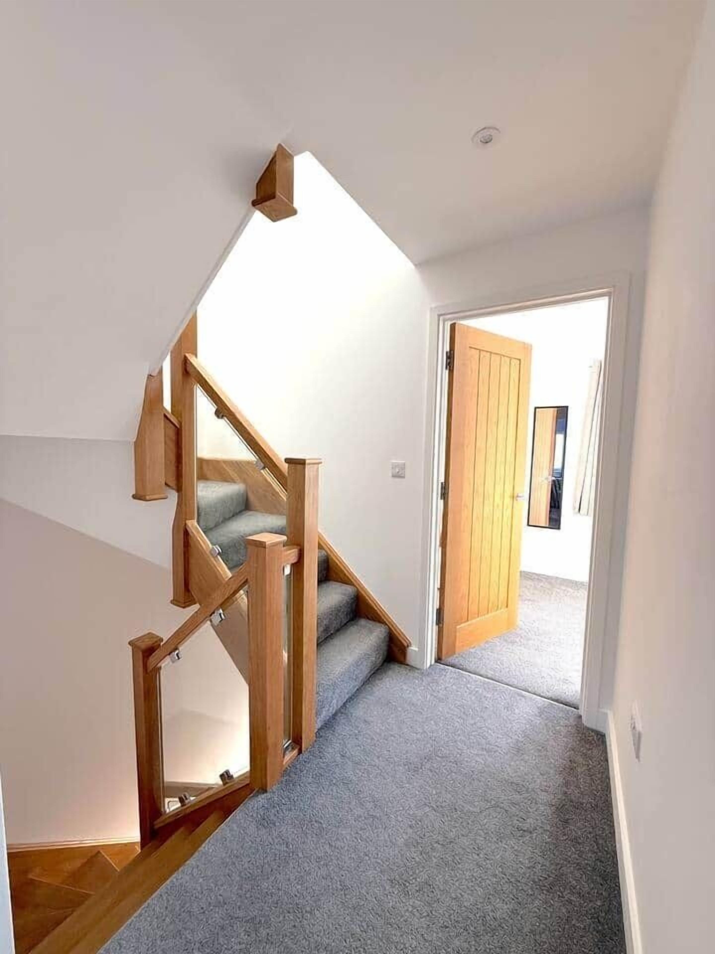 Un escalier avec des rampes en bois et des marches recouvertes de moquette, menant à une porte.