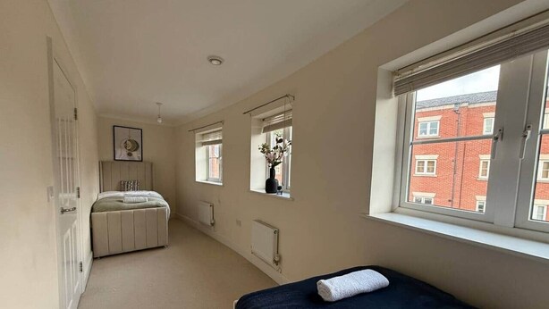 A bedroom with a bed, a window, a radiator, and a door. - Central 5-Bed, 2 En-Suites - Sleeps 12 - Parking (Cheltenham)