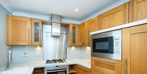 A modern kitchen with wooden cabinets, stainless steel appliances, and a white countertop. - Spacious 5bed in Cheltenham Town (Cheltenham)