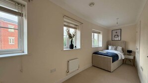 A bedroom with a bed, two windows, a radiator, and a nightstand. - Central 5-Bed, 2 En-Suites - Sleeps 12 - Parking (Cheltenham)