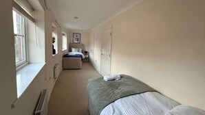 A narrow hotel room with a single bed, a window, a radiator, and a door leading to a bathroom. - Central 5-Bed, 2 En-Suites - Sleeps 12 - Parking (Cheltenham)