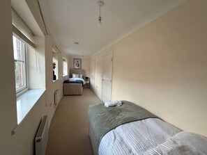 A narrow hotel room with a single bed, a window, a radiator, and a door leading to a bathroom. - Spacious 5bed in Cheltenham Town (Cheltenham)