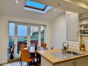 A modern kitchen with a skylight, a dining area with chairs, and a view of the outdoors. - Beautiful Modern Central Home (Cheltenham)