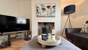 Una sala de estar moderna con un televisor de pantalla plana, una chimenea, una mesa de centro redonda con velas y un sofá negro.