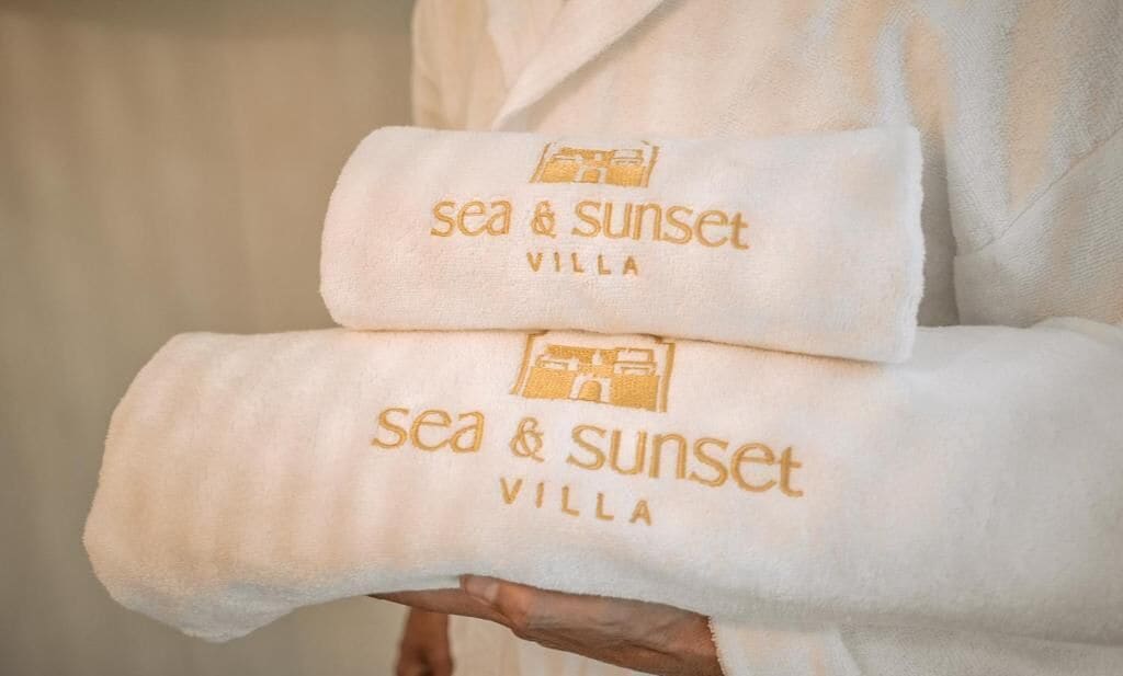A person holding two towels with the text 'sea & sunset villa' embroidered on them.