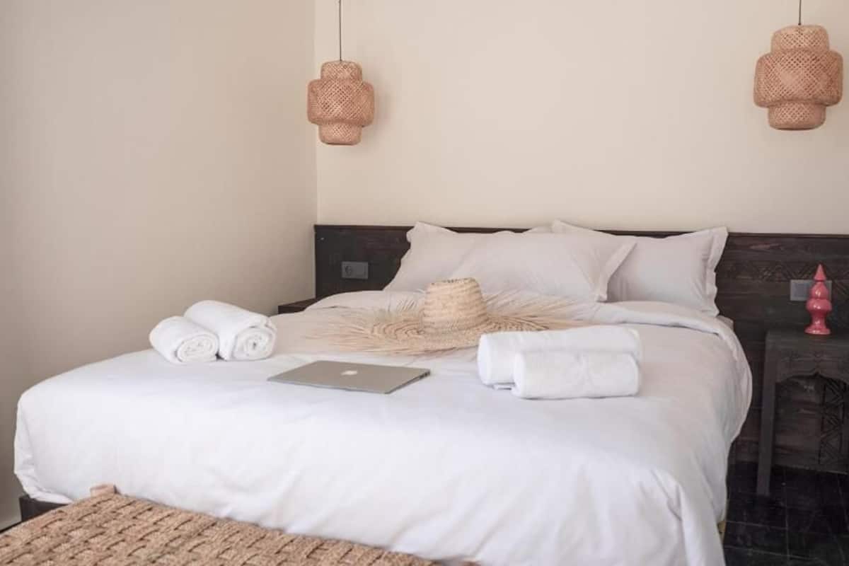 Una cama bien hecha con toallas enrolladas, una computadora portátil y una manta tejida.