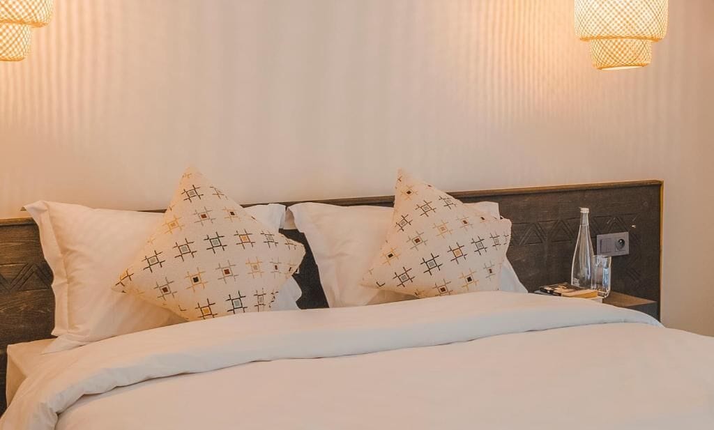 A neatly made bed with patterned pillows, a bedside lamp, and a wall-mounted light fixture.