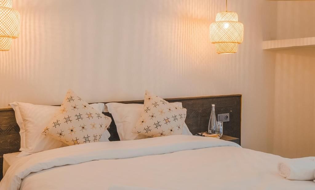 A neatly made bed with patterned pillows, a bedside table with a glass, and two wall-mounted lamps.